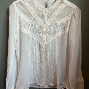Vit blus med spets - Superfin vit blus från Pepe Jeans med broderade detaljer och spetsinslag framtill. Långärmad modell i tunn bomull med knappar hela vägen och romantiska broderier.