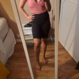 Rosa ribbad omlottopp body med volang - Supersöt rosa omlottopp med djup v-ringning och volangdetaljer på axlarna. Toppen är ribbad och har en figurnära passform som framhäver siluetten. Perfekt för dig som gillar feminina detaljer och en trendig look.