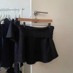 Svart kortkjol från Bikbok  - Supersnygg svart kortkjol från Bikbok med bred linning och lätt utsvängd passform. Kjolen är enkel och stilren, perfekt att matcha med en crop top eller stickad tröja. Materialet känns mjukt och följsamt.