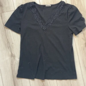 Svart topp med spets och v-ringning - Svart topp med korta ärmar och snygg v-ringning dekorerad med spetsdetaljer. 