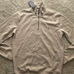Beige half zip tröja från Polo Ralph Lauren - Snygg beige långärmad tröja från Polo Ralph Lauren med half zip och klassisk broderad logga på bröstet. Tröjan har en hög krage och är gjord i mjuk bomull, perfekt för lager-på-lager. Enkel och stilren design som funkar till det mesta. Förlåt för suddiga bilder min kamera är sönder. Det står M på den men den är liten i storlek så den passar S.