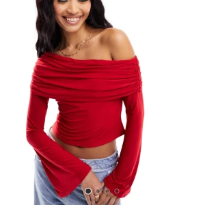 Röd offshoulder croppad tröja - Snygg röd offshoulder topp med långa ärmar och croppad passform. Toppen har draperad överdel och vida ärmslut, vilket ger en trendig och cool look. Perfekt att styla med jeans eller kjol för en statement-outfit.