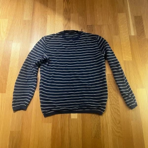 Randig blå tröja från Phil Petter - Snygg långärmad tröja från Phil Petter i marinblått med tunna vita ränder. Klassisk rund halsringning och ribbade muddar. Perfekt för dig som gillar stilrena och tidlösa plagg med lite edge. 100% bomull, made in austria.