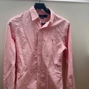 Ralph Lauren skjorta - Säljer en klassisk rosa skjorta från Polo Ralph Lauren i slim fit-modell. Skjortan har långa ärmar, knappar framtill och den ikoniska broderade loggan på bröstet. 