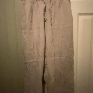 Beiga linnebyxor med snörning - Säljer ett par beiga linnebyxor med avslappnad passform och elastisk midja med snörning. Perfekt till varma dagar. Säljers pga för stora, så inga defekter