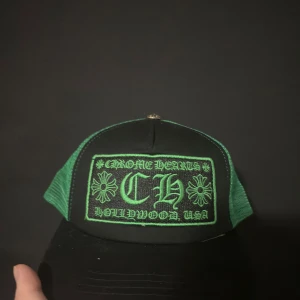 Grön Chrome Hearts keps one size - Snygg truckerkeps från Chrome Hearts i svart och grönt med broderad logga och blommor framtill. Kepsen har mesh på sidorna och baksidan samt en metallknapp med gravyr på toppen. Tillverkad i bomull och polyester.