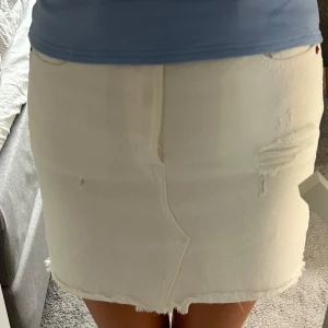 Vit jeanskjol från Levi's med fransad kant - Vit jeanskjol från Levi's med snygga fransar i nederkant och slitna detaljer framtill. Klassisk femficksmodell med knappgylf och bakfickor med Levi's-röd etikett. Snygg och enkel att styla till allt, perfekt för en chill look. Använd en gång och passar även till folk som bär xs/s i vanliga fall!💕💗Pris kan diskuteras