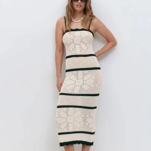 Beige virkad långklänning med blommor - Superfin beige virkad långklänning med svarta ränder och stora blommönster. Klänningen har smala axelband och är figurnära med en snygg boho-vibe. Perfekt för sommardagar eller festivalhäng.