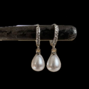 Silverfärgade örhängen med pärldroppar  - Snygga örhängen med glittriga stenar på silverfärgade hoops och droppformade vita pärlor. Perfekta för dig som vill ha en elegant och trendig look med lite extra bling. Rostfri