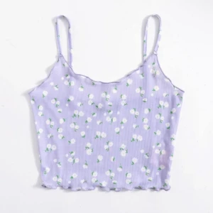Ljuslila blommig croppad linnetopp - Superfin ljuslila croppad linnetopp med vita små blommor och gröna detaljer. Toppen har tunna axelband, ribbad struktur och vågig kant nertill. Perfekt för varma dagar och ger en söt och trendig vibe.