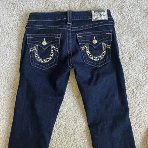 True Religion mörkblå jeans med bling - Mörkblå jeans från True Religion med snygga fickor. Dem passar bra för dig som vill ha ett par lågmidjade jeans. Jag på bilden är 161 cm lång. Midjemåttet rakt över är 40 cm.