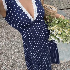 Marinblå prickig långklänning med spets - Superfin marinblå långklänning med vita prickar och v-ringning kantad av vit spets. Klänningen är ärmlös och har en figurnära passform upptill som faller snyggt över kroppen. Perfekt för sommarens alla tillfällen! Tänk er en picknick med med någon ni gillar eller kanske en dejt...😉 det finns även en liten blomma i v ringningen slut. Så gulligt♡♡♡ Den är aldrig använd och själ allas uppmärksamhet!! 💐💐 priset kan diskuteras!! 