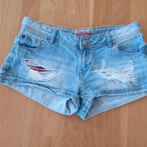 Ljusblå slitna jeansshorts - Snygga ljusblå jeansshorts  med slitna detaljer och klassisk femficksmodell. Perfekta för varma dagar och ger en avslappnad vibe. Shortsen har låg midja och är gjorda i mjukt jeanstyg.