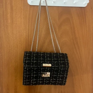 Svart rutig axelväska med kedja -  Svart axelväska med rutigt mönster och guldfärgad kedja som kedja. Säljer eftersom den inte kommer till användning längre