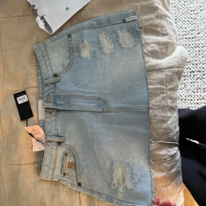 Ljusblå jeanskjol från One Teaspoon - Säljer en helt ny snygg ljusblå jeanskjol från One Teaspoon med slitna detaljer och rå kant nertill. Kjolen har klassiska fickor fram och bak samt. Kontakta om fler frågor! 💞