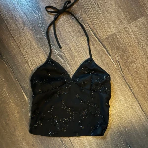 Svart glittrig  topp - Svart halterneck topp med glittriga paljettdetaljer och v-ringning. Den knyts i nacken och är SUPERSNYGG till festliga sammanhang🩷
