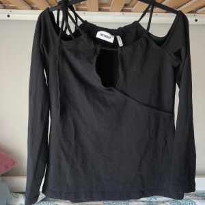 Svart långärmad topp Weekday cut out - Svart långärmad topp från Weekday med cool cut out-detalj framtill och smala axelband som ger en unik look. Toppen har en asymmetrisk öppning vid halsen och är gjord i mjuk bomull. 