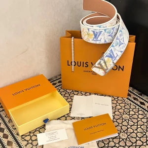 bälte i vitt med färgstänk - Snyggt bälte i vitt skinn med färgstänk i blått, gult och orange Bältet har en silverfärgad spänne och exklusiv känsla. Perfekt för dig som vill sticka ut med en lyxig accessoar.