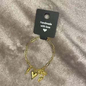 Guldigt armband med berlocker - Charmigt armband i guldton med chunky länkar och tre berlocker: ett hjärta, en rosett och en spetsig kon. Perfekt accessoar för att lyfta din stil med en lekfull och trendig touch. För att armbandet ska hålla sig snyggt så försök att ta av det innan dusch!❤️