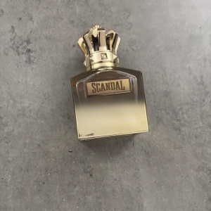 Scandal parfym från Jean Paul Gaultier - Lyxig parfymflaska från Jean Paul Gaultier, Scandal. Flaskan är fyrkantig med en snygg guldig gradient och en unik kronformad kork i metall. Perfekt för dig som gillar statement-dofter och vill ha en snygg detalj på sminkbordet.  90 ml kvar av 100 ml