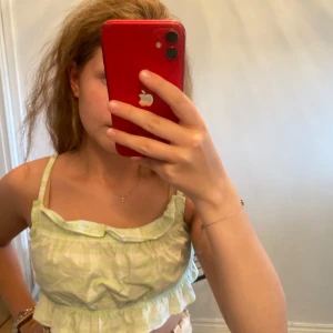 Grön- och vitrutigt croppat linne - Säljer ett sött croppat linne med tunna axelband och volangdetalj upptill. Toppen har ett ljusgrönt och vitt rutigt mönster och är perfekt för varma dagar. Luftigt material och avslappnad passform som ger en chill vibe.