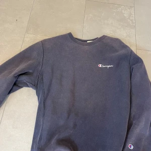 Mörkblå sweatshirt från Champion - Säljer en mörkblå sweatshirt från Champion med broderad logga på bröstet och ärmslutet. Tröjan har rund halsringning och långa ärmar, perfekt för en chill och sportig stil. Klassisk och enkel design som funkar till det mesta.