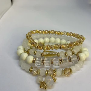 Pärlarmband i vitt och guld - Fyra elastiska armband med vita, klara och guldiga pärlor i olika former och storlekar. Armbanden har detaljer i guld och transparenta pärlor som ger en lyxig och glittrig känsla. Dessa armband är inte använda utan kommer från min small business. 