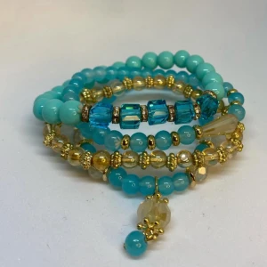 Turkost och guldigt pärlarmband - Flera elastiska armband med turkosa och guldiga pärlor, dekorerade med blåa kubformade pärlor och små gulddetaljer. Ett av armbanden har en hängande pärla som extra detalj. Dessa armband är inte använda utan kommer från min small business. 
