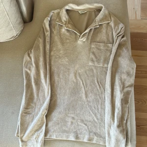 Beige långärmad frotté pikétröja East West - Säljer en beige långärmad pikétröja från East West. Tröjan har klassisk krage, bröstficka och är gjord i mjuk frottéblandning av bomull och polyester. Perfekt för dig som gillar en chill och avslappnad stil.