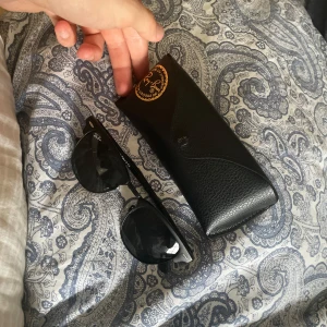 Svarta Ray-Ban Wayfarer solglasögon - Klassiska svarta Ray-Ban Wayfarer solglasögon med snygg, tidlös design. Kommer med original svart fodral med gul Ray-Ban-logga. Perfekta för att lyfta din stil och skydda ögonen mot solen.