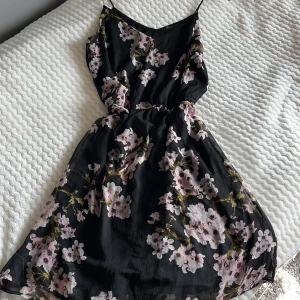 Svart blommig klänning från Vero Moda - Säljer en svart klänning från Vero Moda med vackert blommönster i rosa och vita nyanser. 
