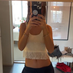 Vit fransig linnetopp - Säljer en vit linnetopp med fransdetaljer längst ner. Toppen är ärmlös och har en croppad passform, perfekt för sommarens varma dagar. Ny-pris:400kr