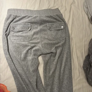 Grå mjukisbyxor från Juicy Couture - Säljer ett par grå mjukisbyxor från Juicy Couture. Byxorna har en bekväm resårmidja med snörning och praktiska fickor både fram och bak. Perfekta för en avslappnad stil.