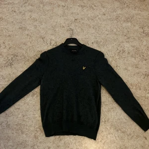 Mörkgrön tröja från Lyle & Scott - Säljer en stilren mörkgrön tröja från Lyle & Scott med ett diskret mönster och deras ikoniska logga på bröstet. Tröjan har långa ärmar och en klassisk rund halsringning. Perfekt för en avslappnad men ändå snygg look.