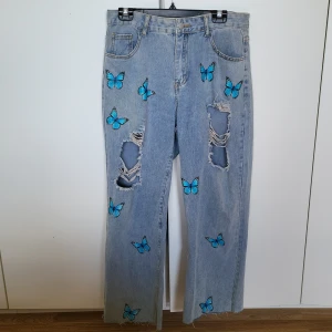 Ljusa jeans med fjärilar - Snygga ljusa jeans med blå fjärilar och slitna detaljer. Byxorna har en rak passform och är dekorerade med fjärilar över hela benen. Perfekta för en unik och trendig stil.