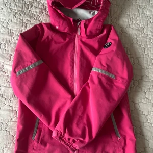 Rosa vindjacka från Polarn O. Pyret - Säljer en snygg rosa vindjacka från Polarn O. Pyret. Jackan har en dragkedja framtill och reflexdetaljer på ärmarna och fickorna. Perfekt för blåsiga dagar med sin skyddande huva och elastiska ärmslut.
