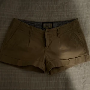 Beige shorts från Abercrombie & Fitch - Snygga beige shorts från Abercrombie & Fitch med klassisk design. De har en knapp och dragkedja framtill samt fickor på sidorna. Perfekta för en avslappnad stil.