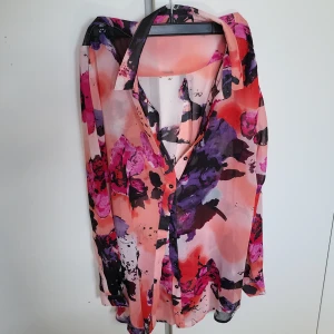 Blommig blus från Fransa - Säljer en färgglad blommig blus från Fransa i storlek M. Blusen har långa ärmar och ett vackert mönster i rosa, lila och svart. Perfekt för att liva upp garderoben!