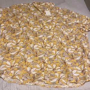 Gul blommig skjorta från Dressmann - Säljer en somrig gul skjorta från Dressmann med ett blommigt mönster i vitt och brunt. Skjortan är kortärmad och tillverkad i ett linneblandat material, perfekt för varma dagar. Den har knappar framtill och en klassisk krage.