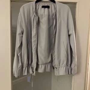 Vårjacka - Säljer en stilren jacka från Zara Basic. Jackan har dragkedja framtill och elastiska detaljer vid midjan och ärmsluten. Perfekt för en avslappnad look. Ljusblå/grå. 