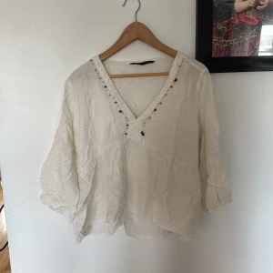 Vit Zara blus med kristall detaljer - En tunn somrig Zara blus med kristall detaljer runt halsen. Luftigt material perfekt för sommaren 