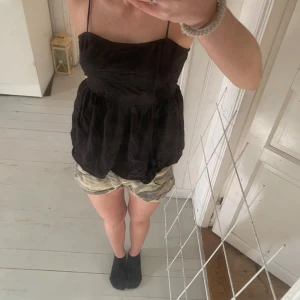 Svart ärmlös topp - Säljer en svart ärmlös topp med smala axelband och en luftig passform. Toppen har en öppen rygg med knytning, vilket ger en snygg detalj. Perfekt för varma sommardagar eller en avslappnad kvällslook.