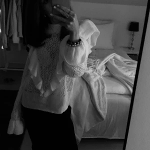 Vit stickad tröja med volangdetaljer - Säljer en vit stickad tröja med vackra volangdetaljer på ärmarna och framsidan. Tröjan har en unik design med ett luftigt stickmönster och långa ärmar. Perfekt för att ge en romantisk touch till din outfit.