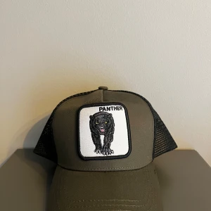 Olivgrön keps med pantermärke - Snygg olivgrön keps med ett coolt pantermärke framtill. Kepsen har ett svart nät baktill för ventilation och en justerbar rem för perfekt passform. Perfekt för en avslappnad stil.