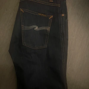 Mörkblå jeans från Nudie Jeans - Snygga mörkblå jeans från Nudie Jeans med klassisk femficksdesign och kontrastsömmar. Jeansen har en rak passform och är tillverkade i högkvalitativt denim. Perfekta för en stilren look.
