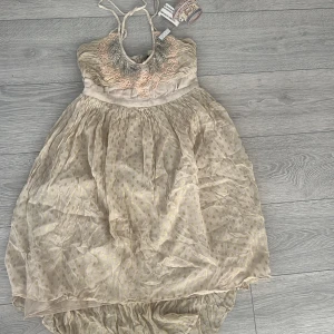 Beige prickig klänning från Frock and Frill - Charmig beige klänning från Frock and Frill med prickigt mönster och paljetter. Klänningen har tunna axelband och en luftig kjol som ger en romantisk känsla. Perfekt för sommarens festligheter!