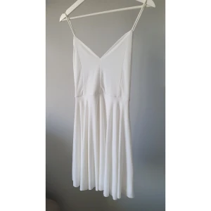 Vit klänning från BikBok - Säljer en stilren vit klänning från BikBok med smala axelband och en v-ringad design. Klänningen har en elegant öppen rygg med korsade banddetaljer. Perfekt till student, skolavslutning, examen eller bara sommarens fina dagar! 🤍