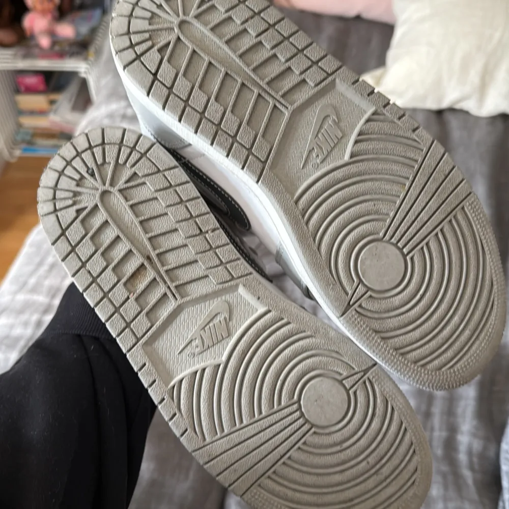 Snygga Nike Air Jordans i grått och vitt med klassisk snörning och hög design. Perfekta för en stilren look med den ikoniska Nike-loggan på sidan. Skorna har en perforerad tå för extra ventilation.. Kengät.