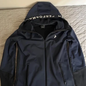 Mörkblå träningströja med huva från peak and formance! - Snygg mörkblå träningsjacka från Peak Performance med dragkedja och huva, strl S i riktigt bra skick. Hör av er ang frågor om tröjan!