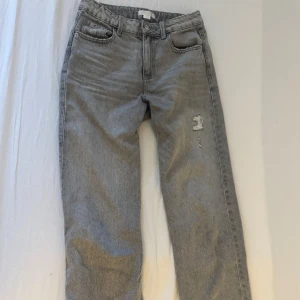 Grå jeans med slitningar - Snygga grå jeans med en avslappnad passform och slitningar på framsidan. De har en klassisk femficksdesign och knappgylf. Perfekta för en casual look.
